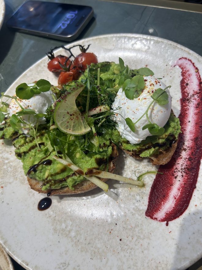 Avocado toast with poached egg, vine tomatoes and herbs on a speckled plate