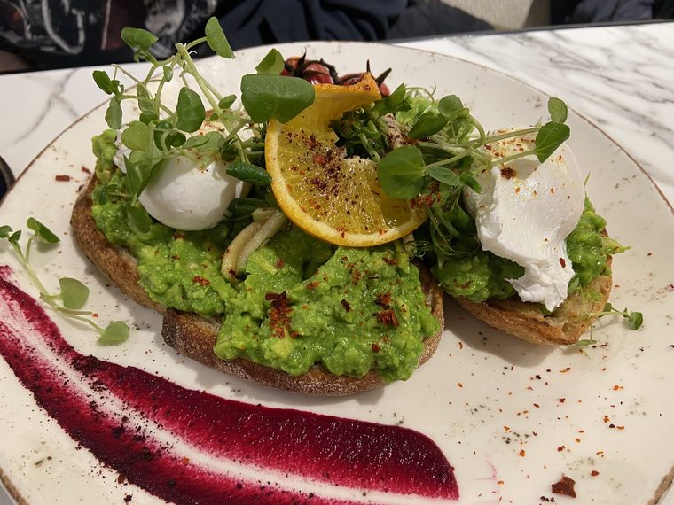 Smashed avocado on toast with poached eggs, microgreens and a lemon wedge