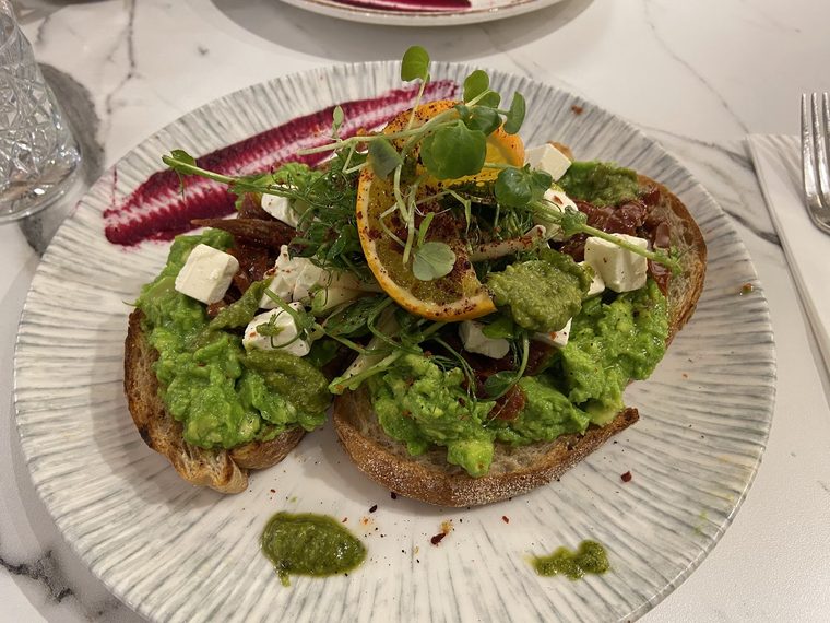 Avocado toast with feta, radish, orange segments and a pesto drizzle